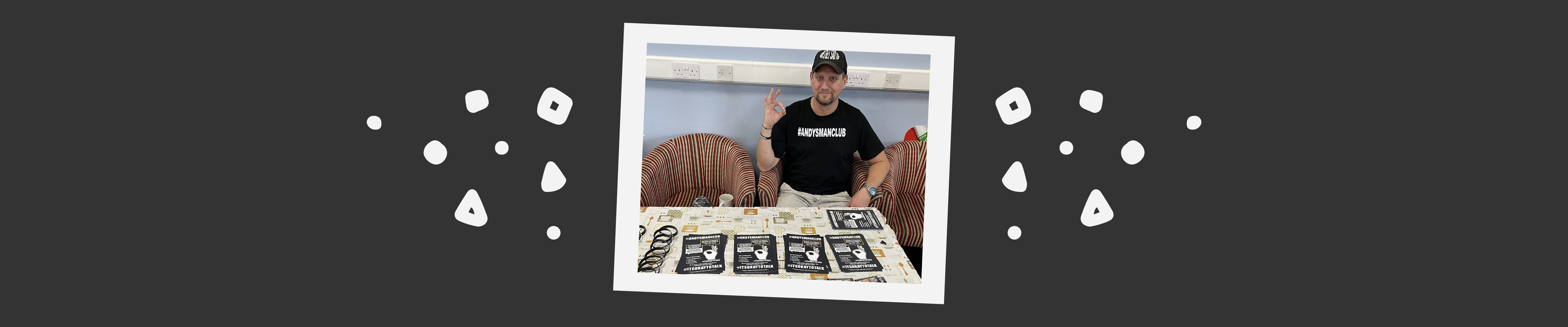 Danny from ANDYSMANCLUB sat at a desk with some #ITSOKAYTOTALK merchandise